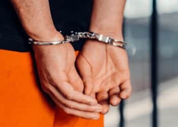 Persoon in handboeien na aanhouding, met handen op de rug en oranje kleding