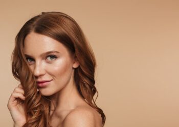 Van Marilyn tot TikTok: hoe ons schoonheidsbeeld is verschoven 4 Vrouw met golvend rood haar en subtiele make-up poseert zelfverzekerd tegen een neutrale achtergrond, beeld voor veranderende schoonheidsidealen