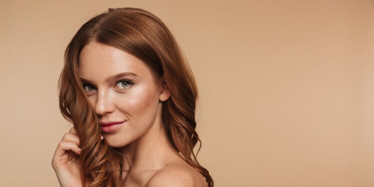 Van Marilyn tot TikTok: hoe ons schoonheidsbeeld is verschoven 1 Vrouw met golvend rood haar en subtiele make-up poseert zelfverzekerd tegen een neutrale achtergrond, beeld voor veranderende schoonheidsidealen